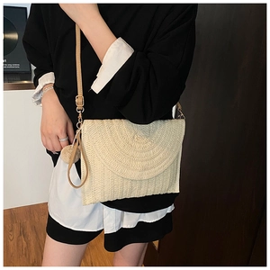 Détail de la pochette en paille tissée avec pompon doux et bandoulière fine pour l'été