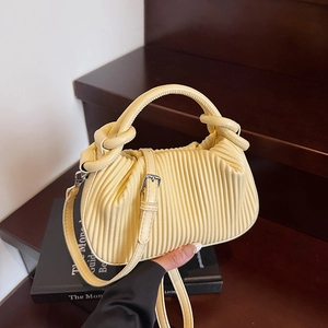 Close-up of light yellow pleated handbag with cylindrical handle and metal strap detail