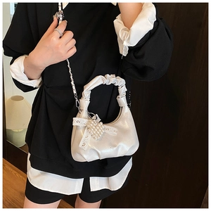Detail of a pearl white pleated handbag featuring a lace bow and pearl charm ornament