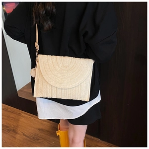 Détail du sac bandoulière en paille beige avec texture tressée et pompon décoratif