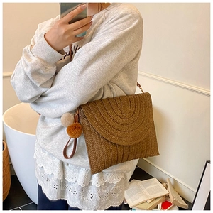 Détail d'un sac à main en paille tressée marron avec pompon bohème et anse en cuir