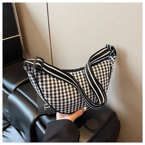 Detail of checkered crescent bag featuring striped shoulder strap and black leather trim
