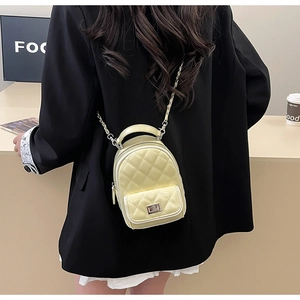 Detail of a pale yellow quilted patent leather mini backpack with metal chain strap
