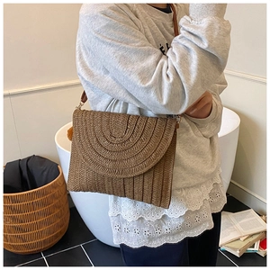 Détail d'un sac bandoulière en paille tressée marron avec rabat à texture circulaire
