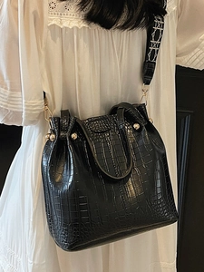 Black crocodile pattern bucket bag with rivet decor and wide geometric woven shoulder strap