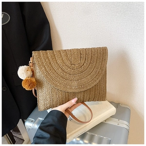 Détail du sac enveloppe en paille tressée marron avec pompons et une longue bandoulière