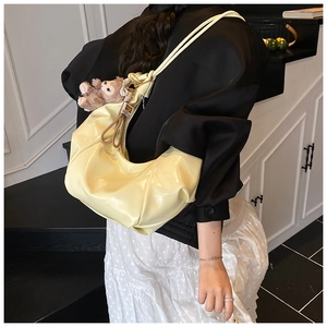 Detail of light yellow crescent hobo bag with glossy finish and cute brown plush bear charm