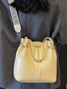 Creamy yellow bucket bag with crocodile texture and woven strap shown on shoulder
