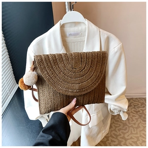 Gros plan sur un sac enveloppe en paille marron avec des pompons décoratifs