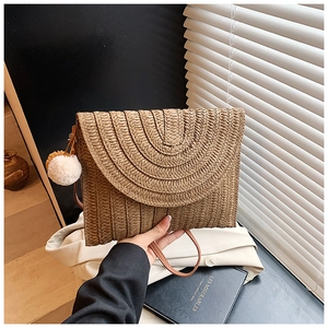 Détail d'une pochette enveloppe en paille tressée marron avec texture ronde et pompon blanc