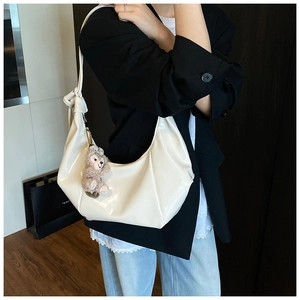 Detailed view of cream crescent shoulder bag with glossy finish and plush bear charm