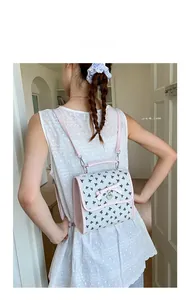 Nahaufnahme eines weißen Mini-Rucksacks mit schwarzen Schleifen und rosa Herzanhänger