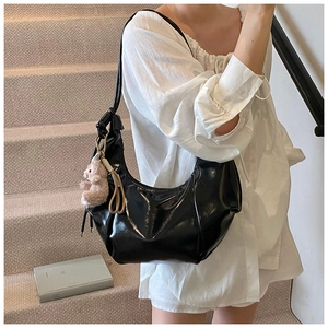 Detail of glossy black hobo bag featuring soft pleats and a cute beige plush bear charm