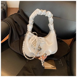 Detail of white pleated dumpling bag with pearl charms and lace bow on leather seat