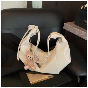 Detail of cream pleated shoulder bag featuring a knot handle and a cute plush bear charm