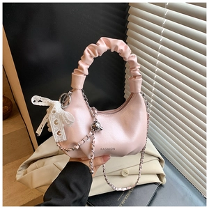 Detail of pink dumpling bag featuring ruffled handle and pearl lace bow charm