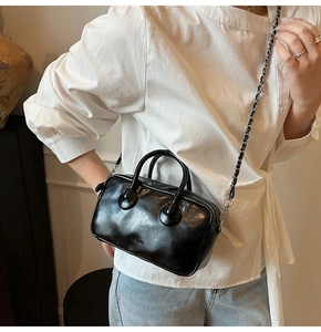 Detailed view of black patent leather bowling bag with chain strap worn by a model