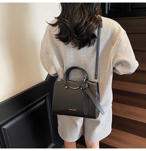 Detail of black leather tote bag with gold metal handle and decorative knotted leather strap