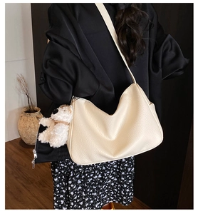 Macro detail of cream-colored shoulder bag with lychee texture and cute plush dog pendant