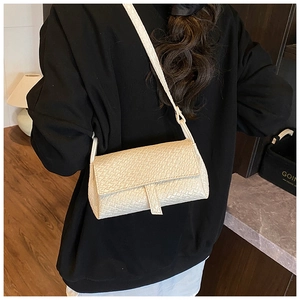 Detail of minimalist beige woven texture shoulder bag worn by model in home setting