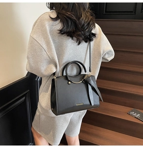 Vue latérale détaillée du sac cabas en cuir noir avec poignées anneaux dorés sur escalier