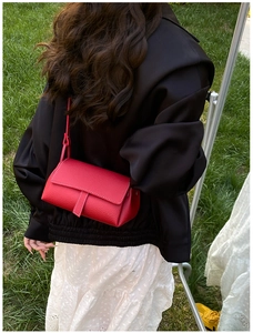 Detailed texture of red lychee pattern leather flap bag worn by model on grass