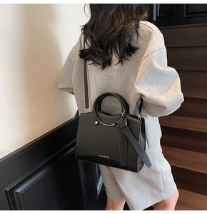 Chic black matte leather tote bag featuring gold lettering and metal ring detail