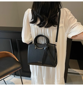 Detail of black leather tote bag with metal ring handle and decorative bow accent