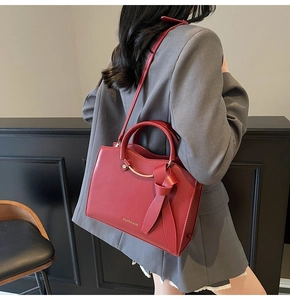 Detailed view of red leather tote bag with gold ring handle and side bow decoration