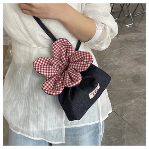 Detail of denim crossbody bag featuring a 3D red gingham flower and Yes Honey label