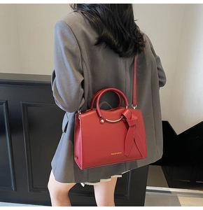 Model showing a large red tote bag with a bow accent and a logo against a grey suit
