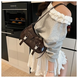 Dettaglio di una borsa sottobraccio marrone scuro lucido con fibbie e doppie tasche frontali