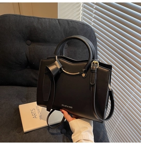 Detail of black PU leather tote with metal ring handles and decorative bow accent