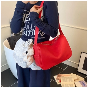 Detail of red pebbled leather underarm bag featuring a white plush puppy charm and zipper