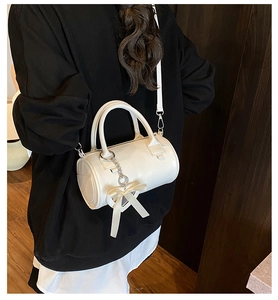 Detailed view of a white cylindrical handbag featuring a silver clasp and a heart charm