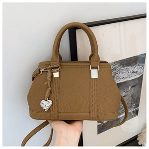 Macro shot of khaki lychee grain leather texture with a silver heart-shaped charm on the bag