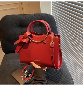 Detailed view of the red tote bag featuring gold ring accents and a large side bow