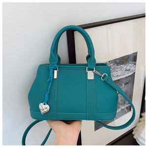 Detail of teal lychee grain leather handbag with silver heart pendant and woven strap