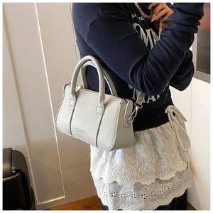 Close-up of light gray lychee grain leather handbag with adjustable strap and metal hardware