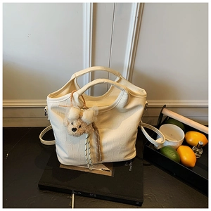 Detail der elfenbeinfarbenen Handtasche mit Krokodilprägung und Plüschbär-Anhänger