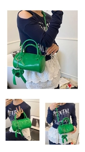 Detailed side view of green cylinder bag with heart bow charm and adjustable strap