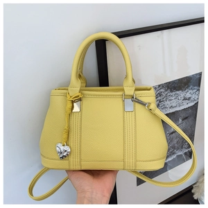 Detail of lychee pattern leather handbag in yellow with silver heart pendant and strap