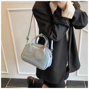Détail du sac bandoulière en cuir bleu clair poli porté avec un blazer noir chic