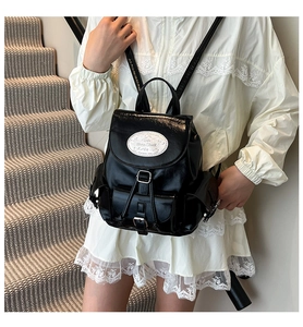 Détail du sac à dos noir brillant avec boucles métalliques et emblème blanc sur des escaliers