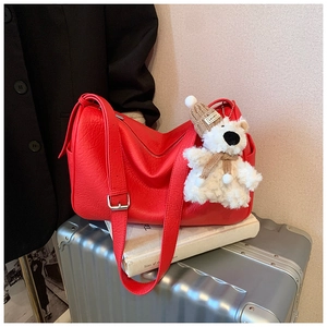 Close-up of a red leather shoulder bag featuring a cute white teddy bear plush charm