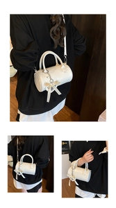 Detailed views of a white cylindrical Boston bag with bow pendant and crossbody strap