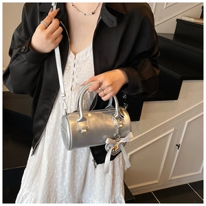 Detail of silver metallic barrel bag with bow heart pendant and adjustable strap