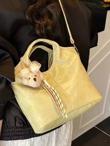 Hellgelbe Eimer-Tasche mit Krokodilmuster und Bärenanhänger von einem Model getragen