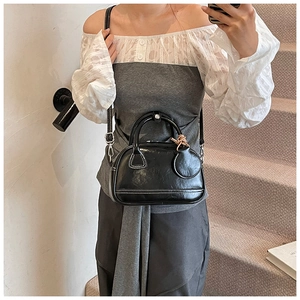 Détail du sac à main noir brillant avec surpiqûres blanches et pendentif rond sur l'escalier