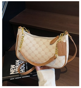 Detail of monogram shoulder bag with gold chain on dark wooden steps and book